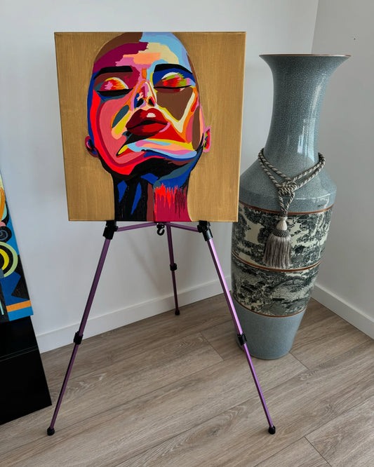 Vibrant abstract portrait painting on an easel, displayed beside a tall ceramic vase in a minimalist interior setting.